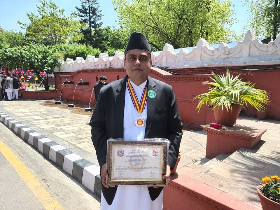 Dr. Niraj Kumar Singh wearing a Nepali state decoration and holding the accompanying framed certificate, in daura suruwal and dhaka topi.