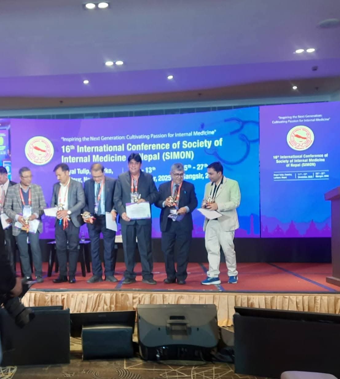A line of physicians holding certificates and trophies on stage at SIMON 2025.